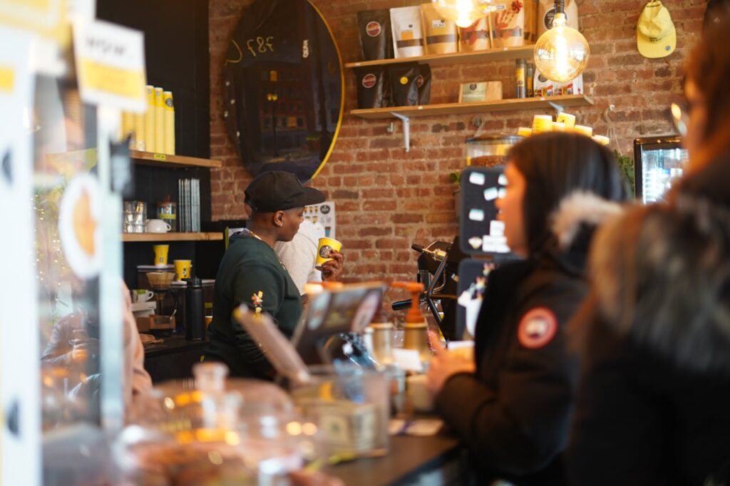 Drukke koffiebar met klanten en een barista, benadrukt interactie en lokale gemeenschap binnen de betekeniseconomie.